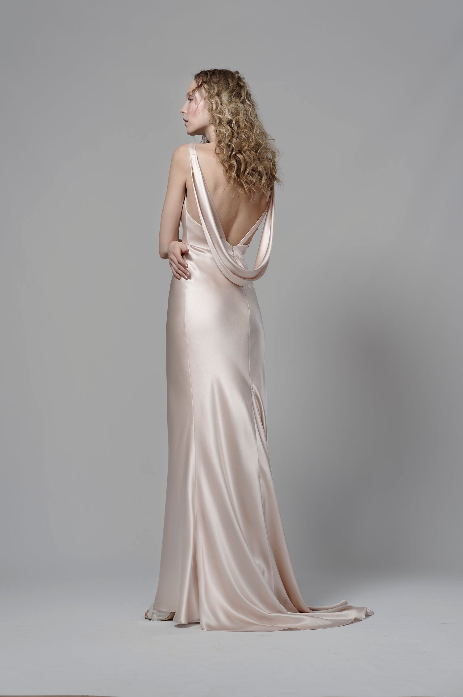 Woman wearing a elegant gown with a draped back design on a plain background