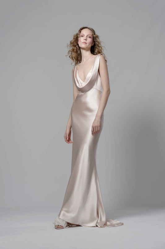 Woman wearing a long, elegant dress with a deep neckline against a plain background