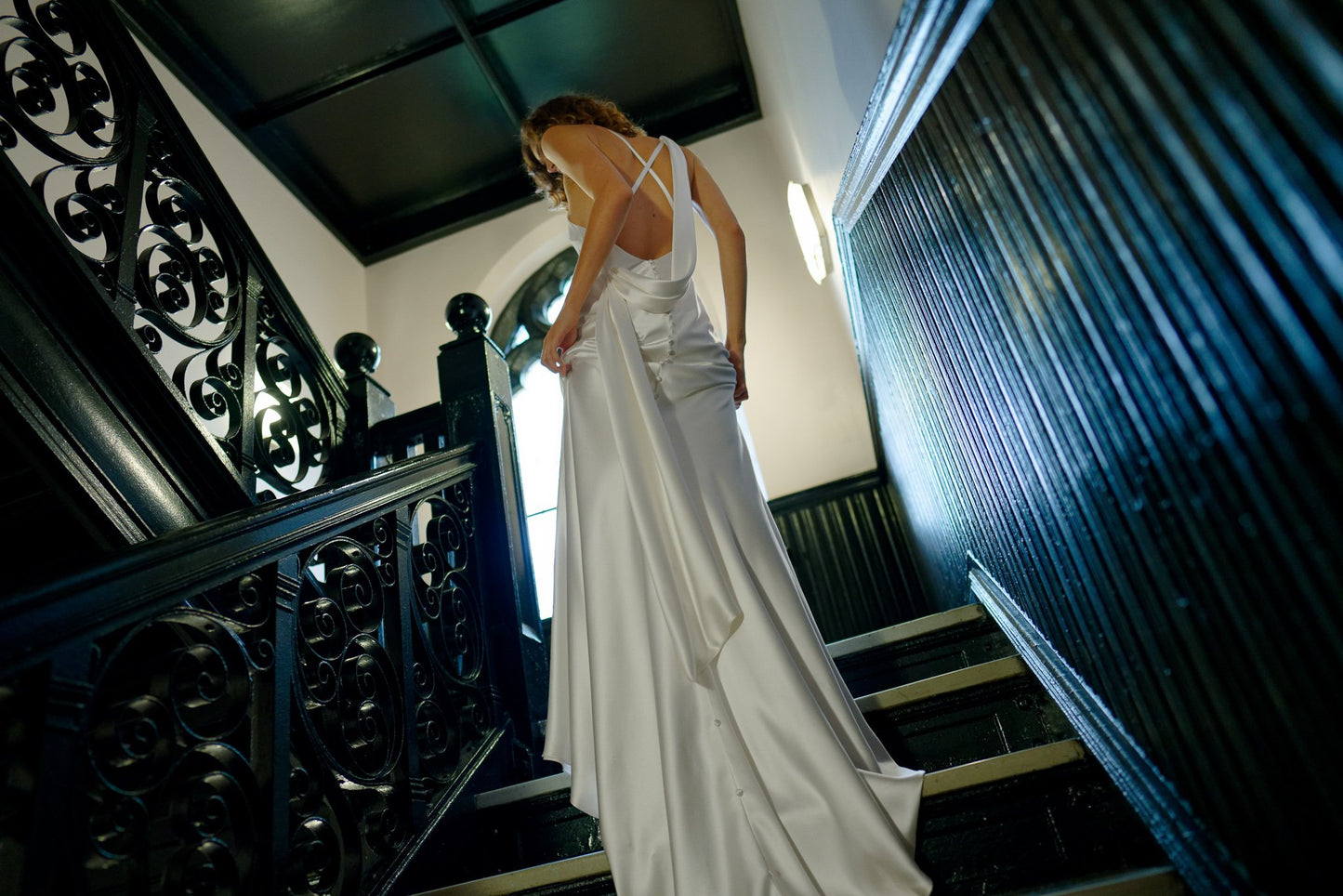 Woman in a white dress standing on a staircase with ornate railings.