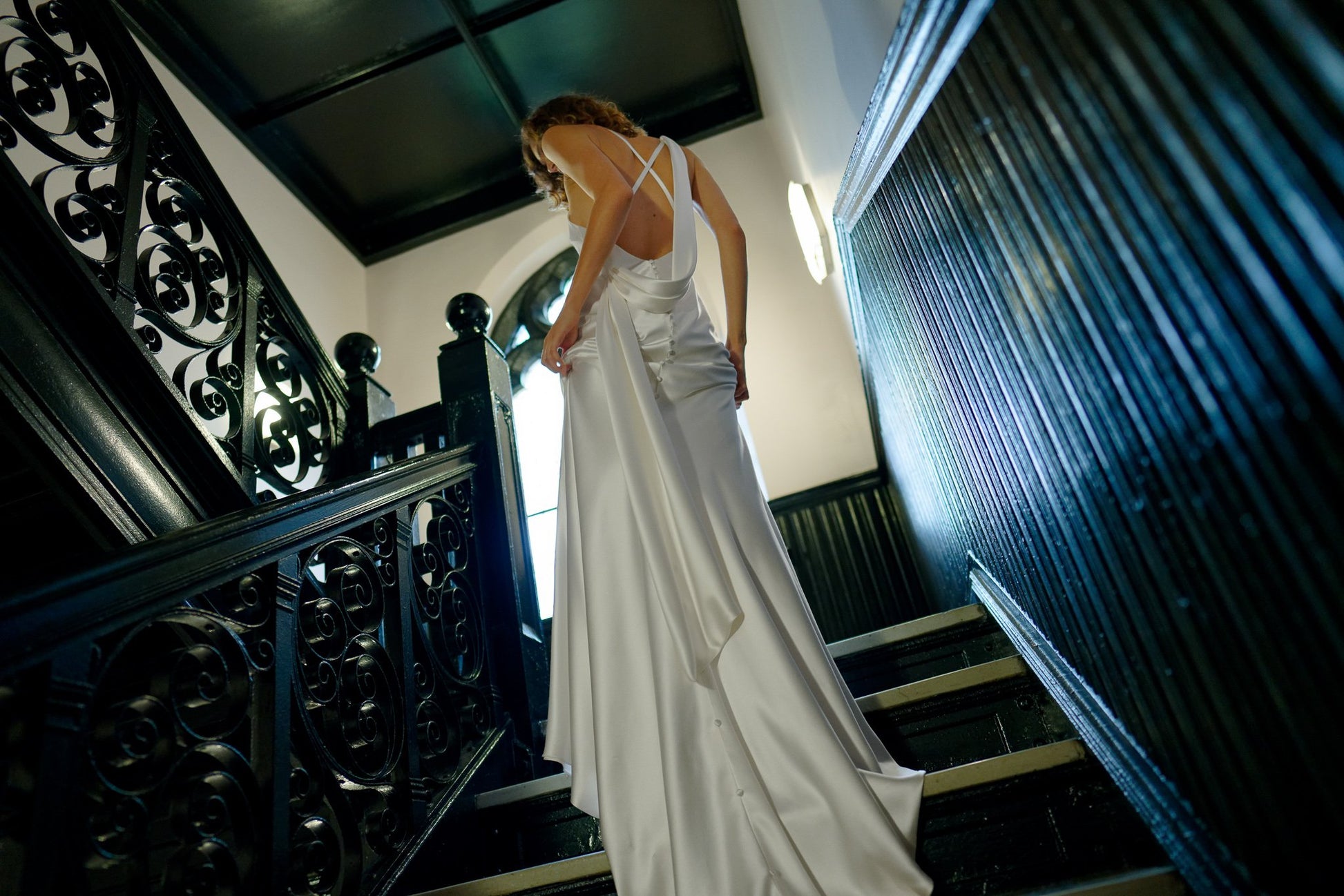 Woman in a white dress standing on a staircase with ornate railings.