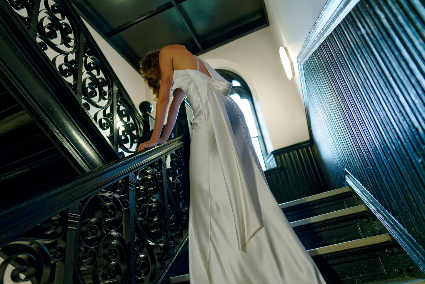 Person in a white dress standing on a staircase with ornate railings.