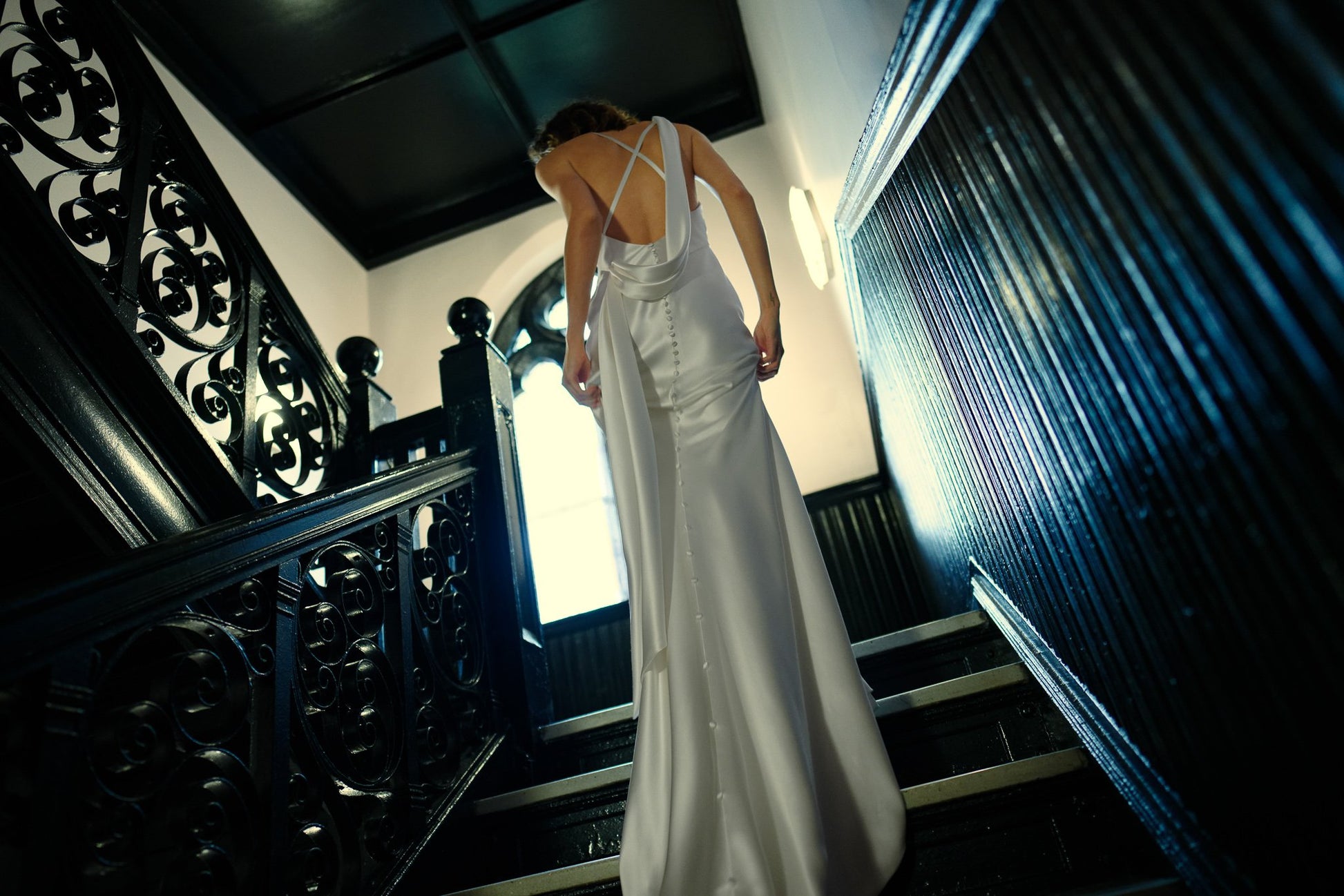 Woman in a white dress standing on a staircase in a dimly lit room.