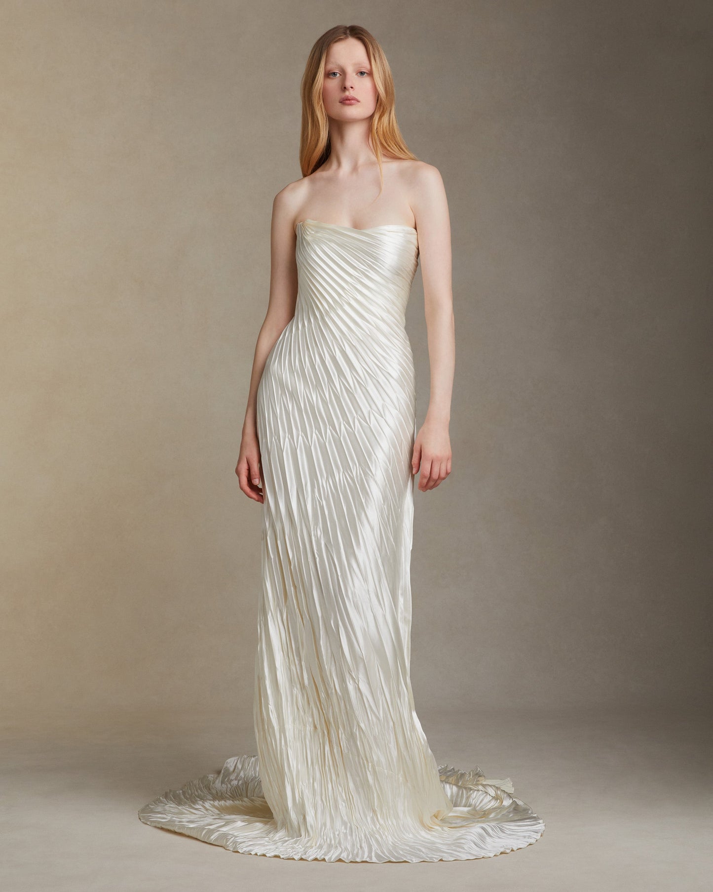 Woman wearing a strapless, pleated white gown against a neutral background