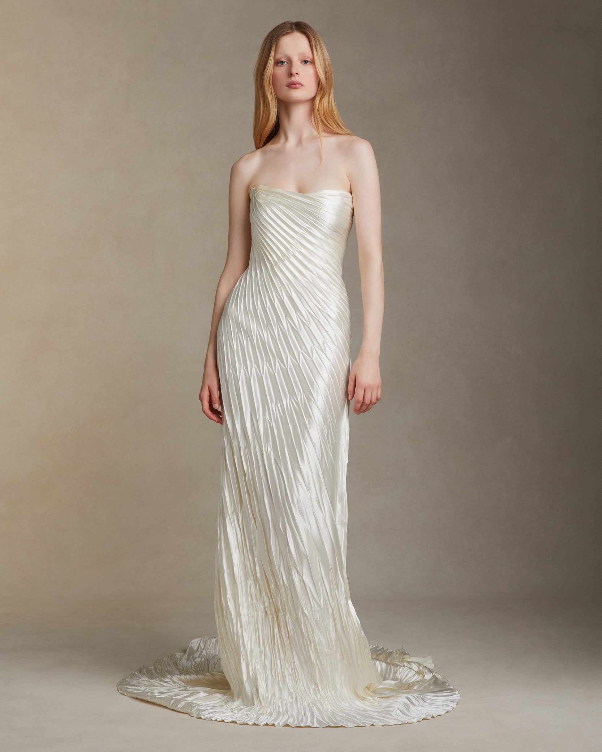Woman wearing a strapless, pleated white gown against a neutral background