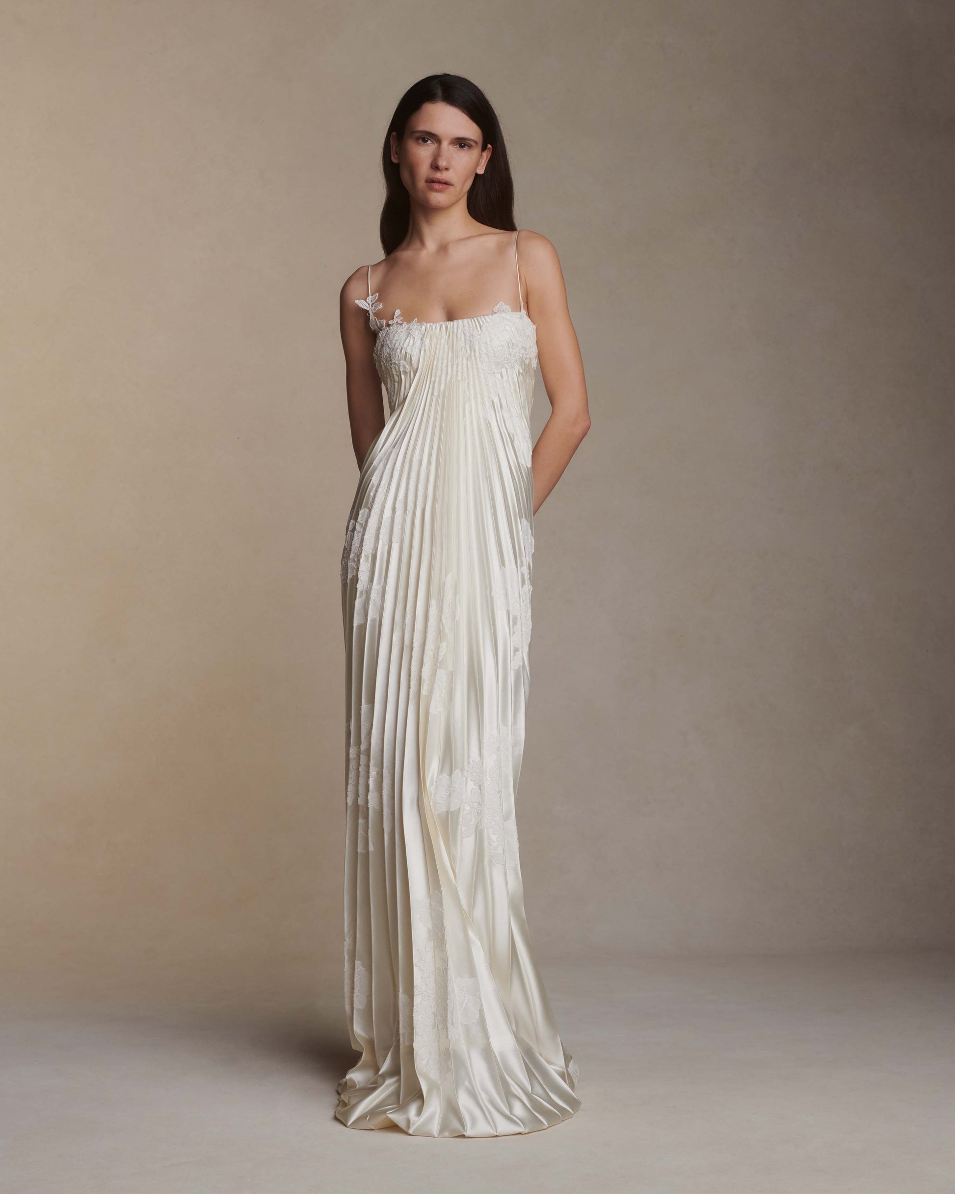 Woman wearing a long, elegant white dress against a plain background