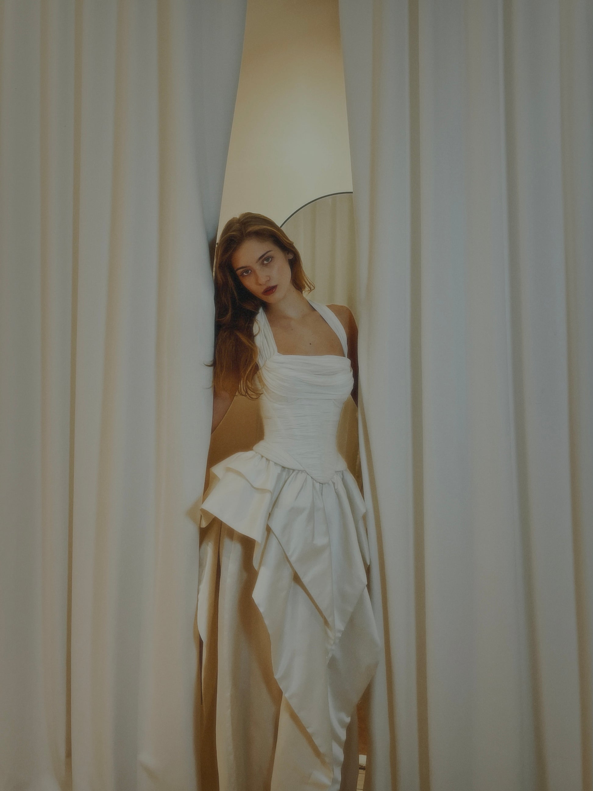 Woman in a white dress standing behind a curtain