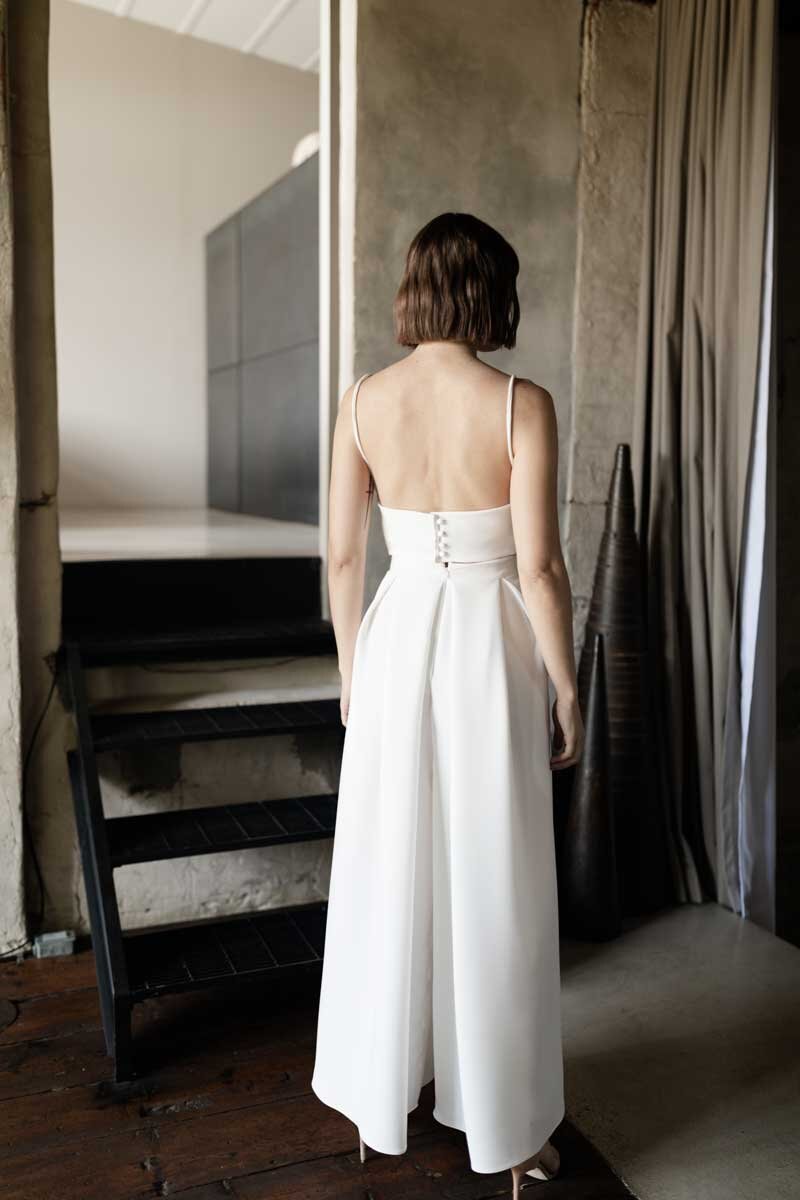 Woman in a white dress standing in a room with concrete walls and a staircase.