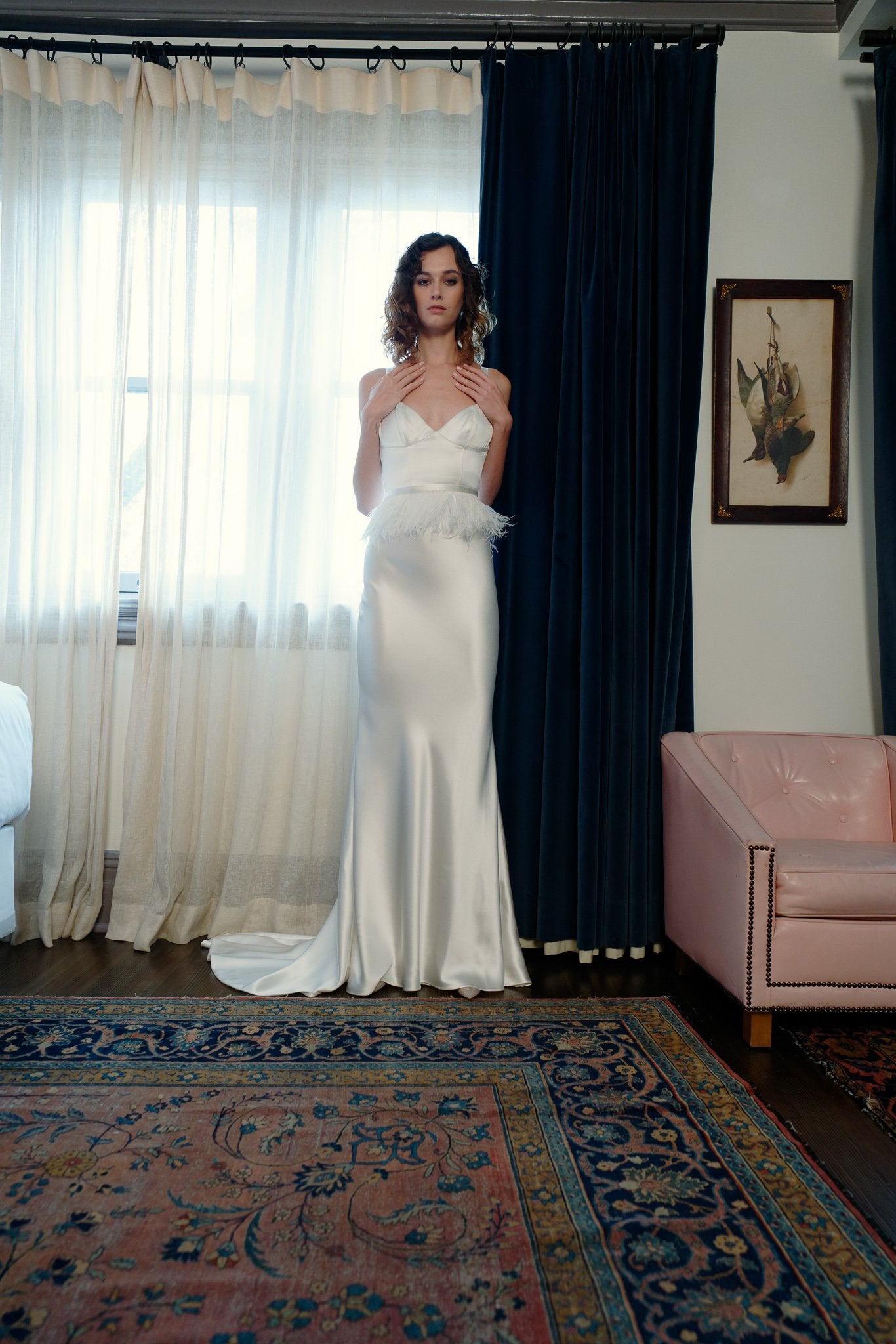 Model wearing the Veronika satin back crepe corset bralette sheath gown standing in a softly lit room with curtains and vintage decor