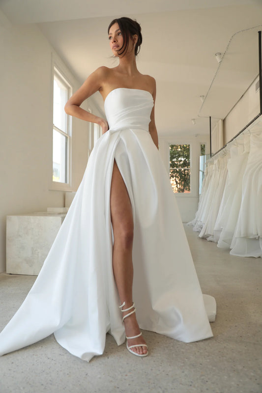 Model wearing the Vivianna strapless silk faille gown with draped waist and high slit in a bright bridal boutique