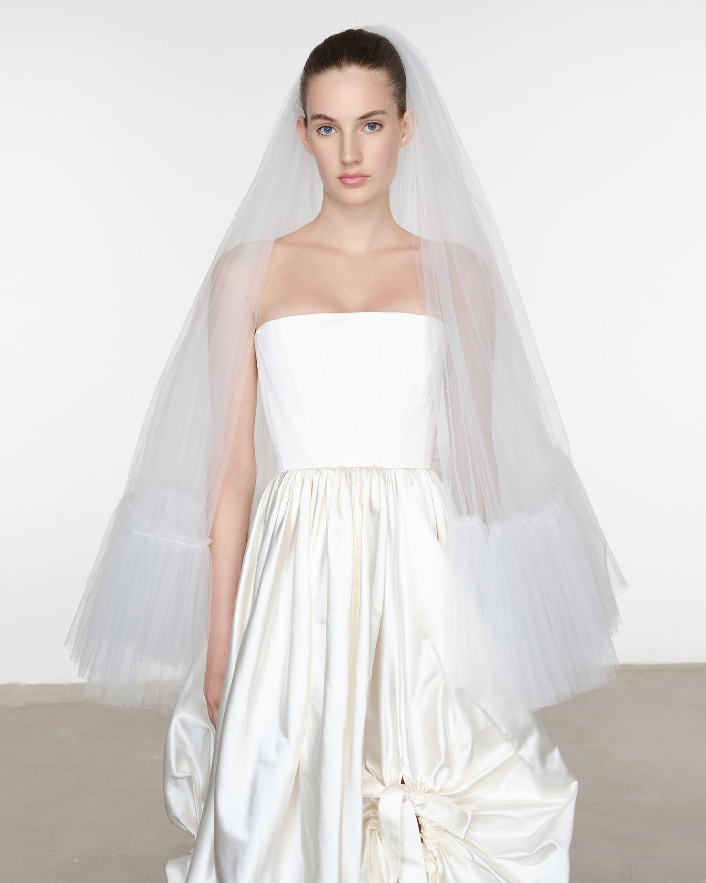 Model wearing a strapless white wedding dress with a long veil against a plain background