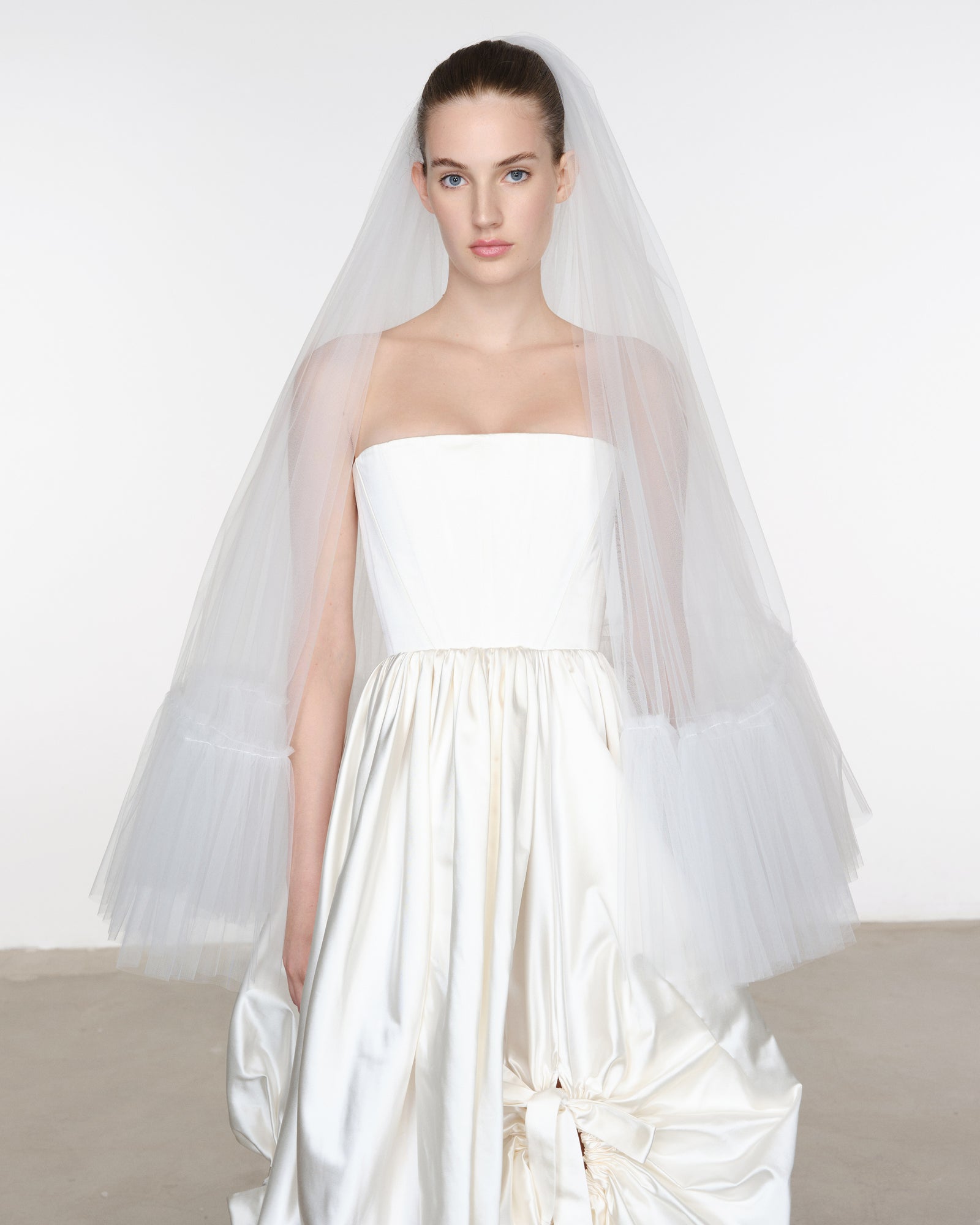 Model wearing a strapless white wedding dress with a long veil against a plain background
