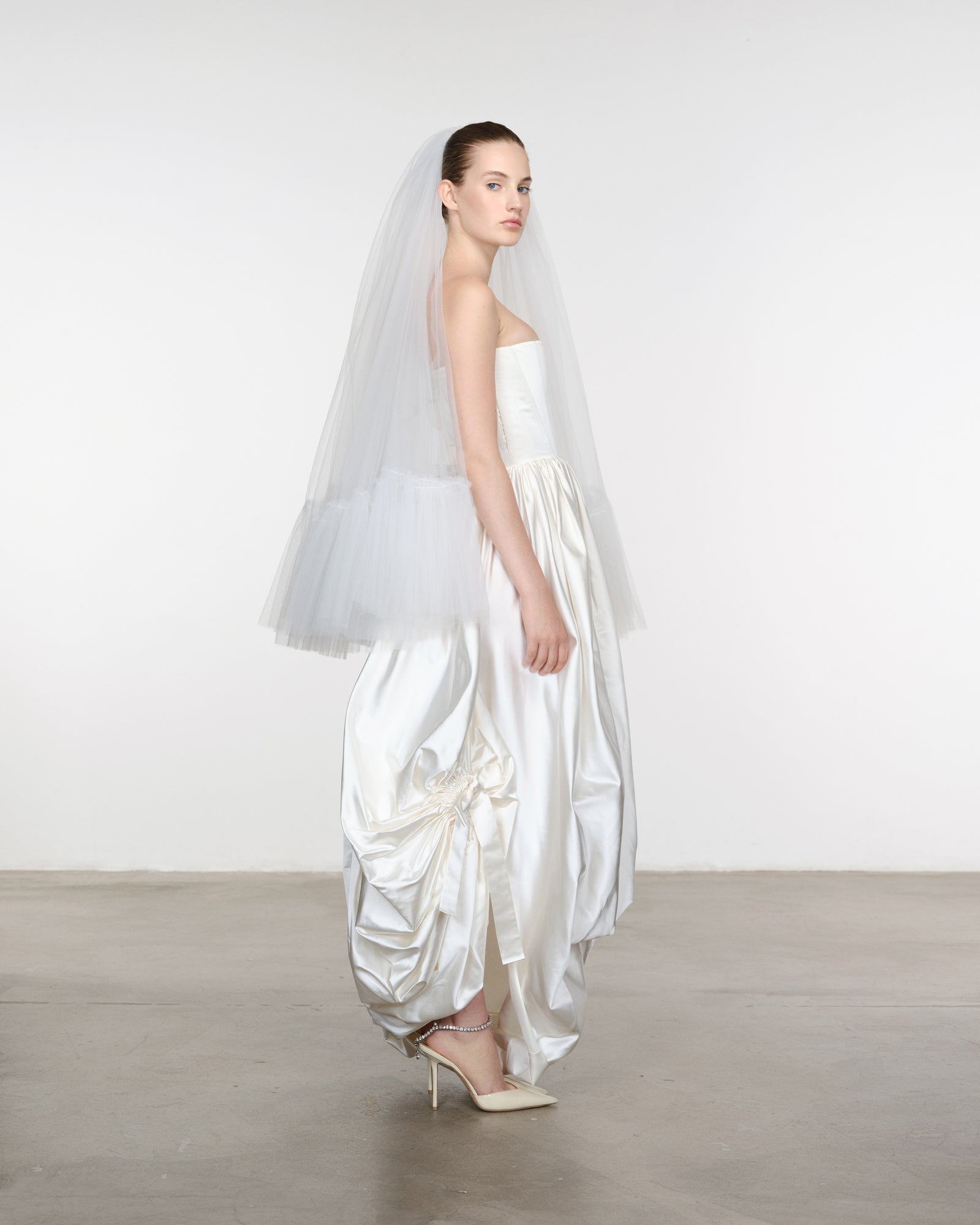 Model wearing a white wedding dress with a veil against a plain background
