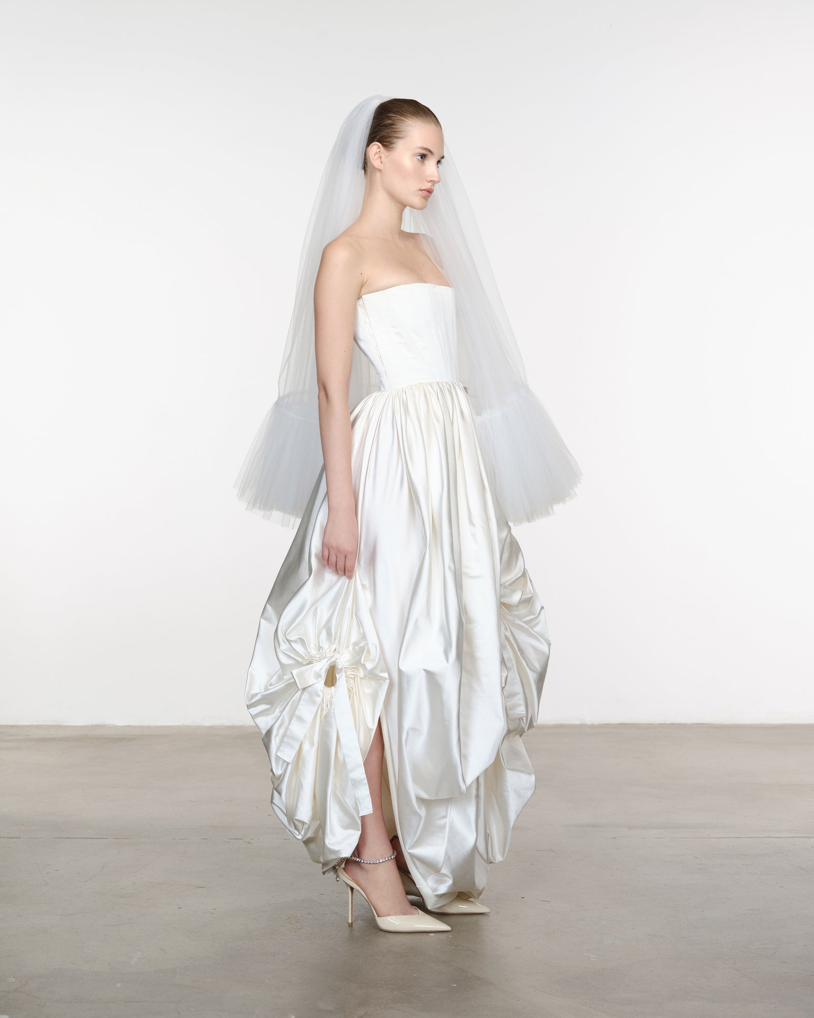 Model wearing a white strapless gown with ruffled skirt and veil against a plain background