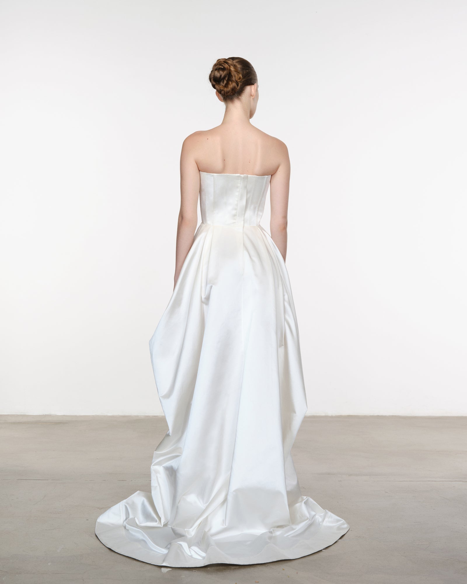 Woman wearing a strapless white wedding dress with a plain background