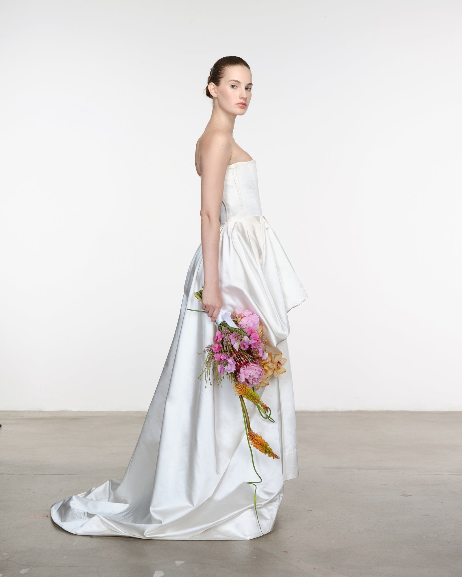 Woman in a white strapless gown holding a bouquet of flowers against a plain background