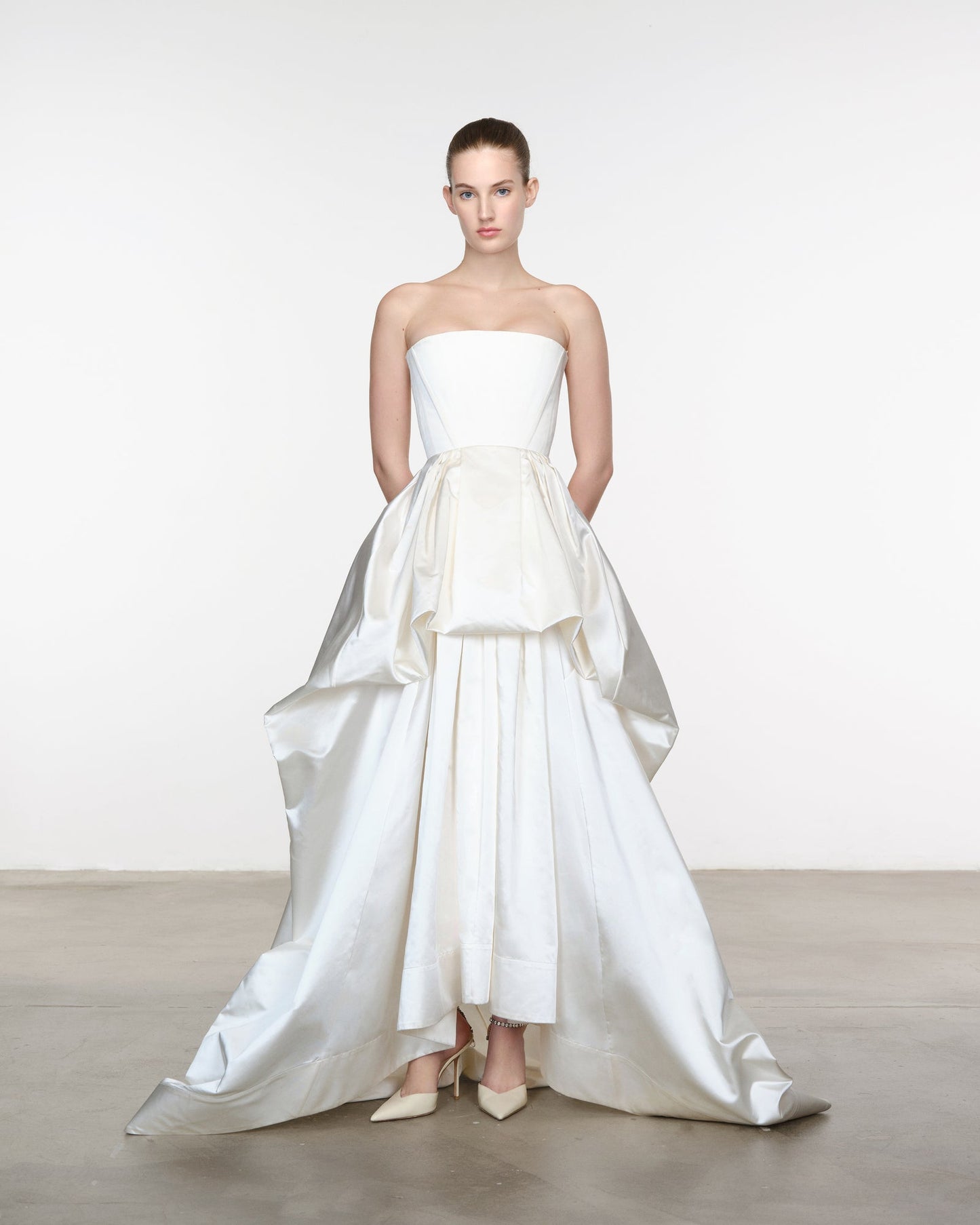 Model wearing a strapless white wedding dress with a layered skirt on a plain background