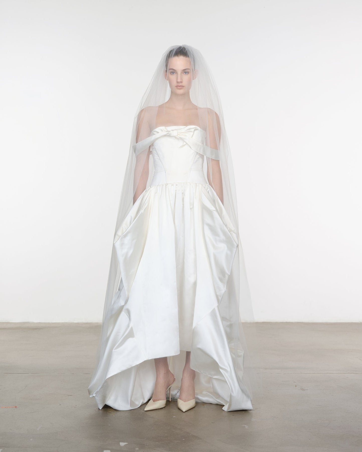 Model wearing a white strapless gown with a long train and veil against a plain background
