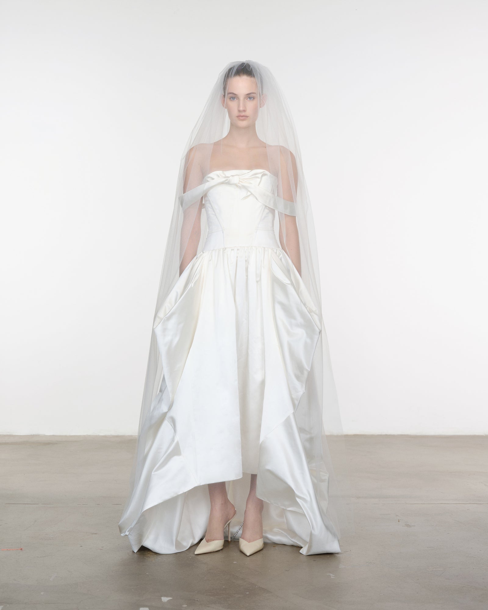 Model wearing a white strapless gown with a long train and veil against a plain background