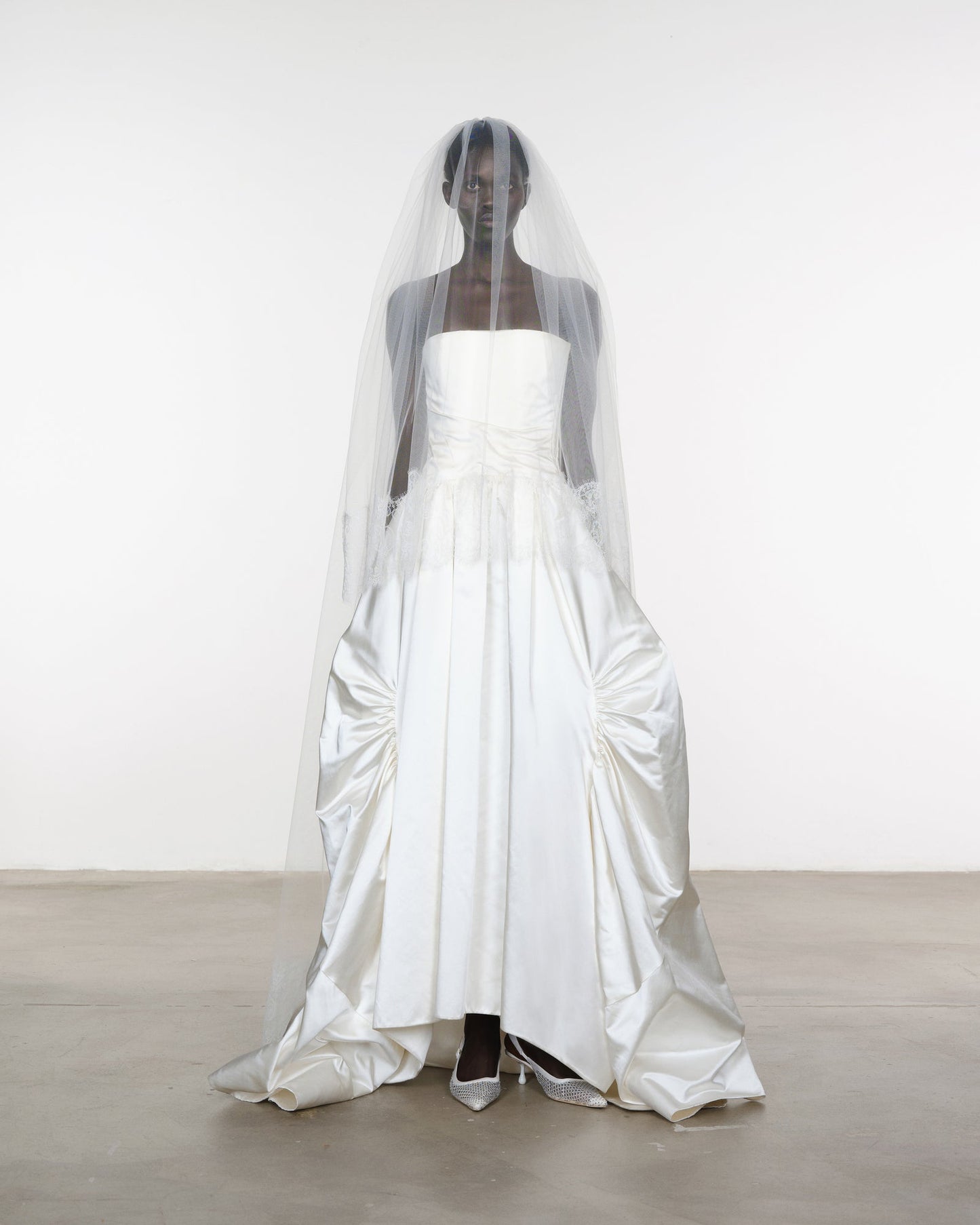 White wedding dress with a long veil on a mannequin against a white background