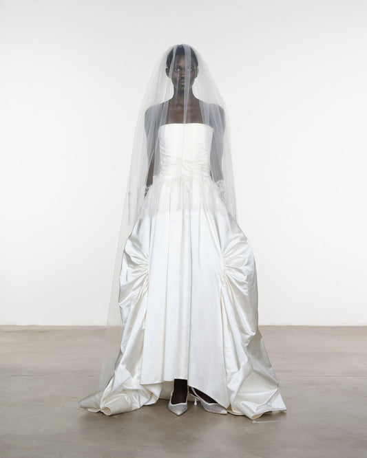 White wedding dress with a long veil on a mannequin against a white background