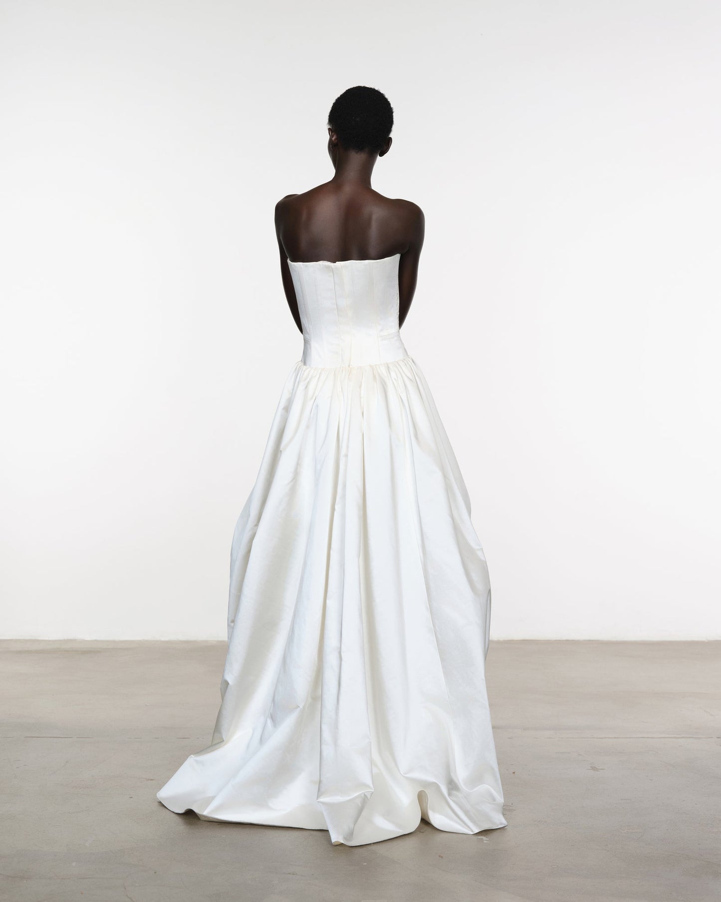 Woman wearing a strapless white wedding dress against a plain background